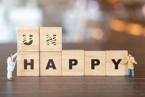 Miniature people, team of workers on wooden blocks with the word Unhappy with the prefix un- crossed-out, leaving the word happy photo