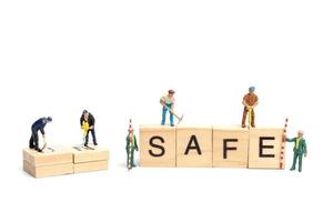 Miniature people, team of workers changing the word Unsafe turned into Safe on white background photo