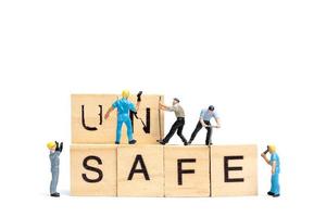 Miniature people, team of workers changing the word Unsafe turned into Safe on white background photo