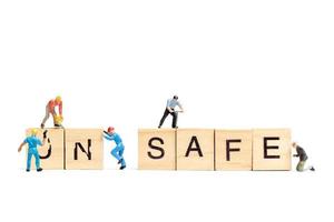 Miniature people, team of workers changing the word Unsafe turned into Safe on white background photo