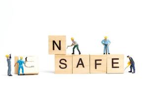 Miniature people, team of workers changing the word Unsafe turned into Safe on white background photo