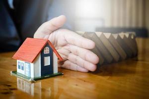 Close up businesswoman with hand in between a house and wooden blocks, stopping risk from everything, security, and insurance concept. photo