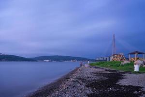 View of rocky shoreline with Russky Bridge in the background and a body of water in Vladivostok, Russia photo