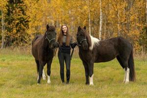 Young Swedish woman in a autumn colored field with her two Icelandic horses