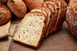 Heap of whole and sliced fresh baked bread on wooden background photo