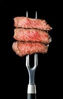 Fresh grilled steak on fork on black background photo