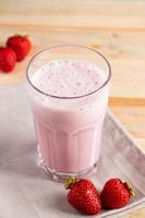 Milkshake with strawberries. Cold summer drink with berries on wooden background. photo