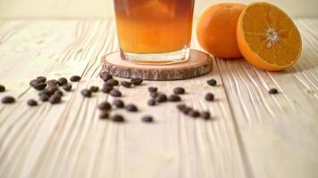 un bicchiere di caffè nero americano ghiacciato e uno strato di arancia decorato con rosmarino e cannella
