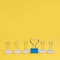 Arrangement of paper clips with one blue paper clip on yellow background photo