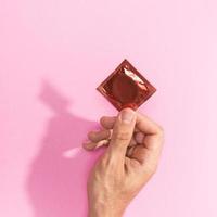 primer plano, hombre, tenencia, arriba, paquete de condón rojo sobre fondo rosa foto