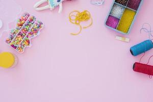 Colorful beads and case of yarn spools on pink background photo