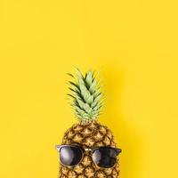 Bright yellow background of a pineapple wearing sunglasses