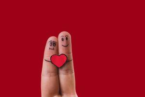 Fingers with drawn faces and a red heart on red background photo