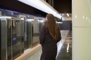una niña con una mascarilla quirúrgica mantiene la distancia social en una estación de metro foto