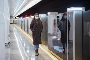 Woman in a medical face mask is standing near the departing train on the subway photo