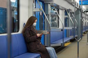 A woman in a face mask is sitting and using a smartphone in a modern subway car