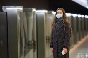 una mujer con una mascarilla médica está esperando un tren y sosteniendo un teléfono inteligente foto