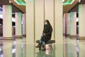 A woman in a medical face mask is waiting for a train and holding a smartphone photo