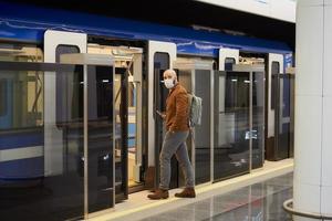 A man in a medical face mask is holding a smartphone while entering a subway car photo