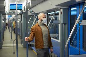 Un hombre calvo con barba en una mascarilla está sosteniendo el pasamanos en un vagón de metro foto