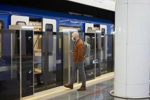 Un hombre con una mascarilla médica sostiene un teléfono inteligente mientras ingresa a un vagón de metro