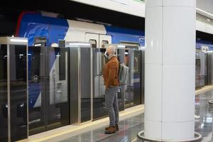 A man in a face mask is holding a smartphone while waiting for a subway train photo