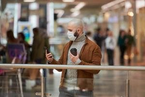Man in a face mask is using a phone and holding a coffee in the shopping center photo