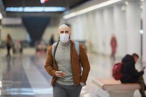 A man in a face mask is using a smartphone while waiting for a subway train photo