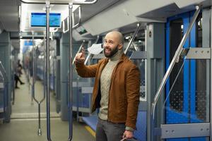 A man with a beard is taking off a medical face mask and smiling on a train photo