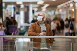 A man in a face mask is holding a cup of coffee in the shopping center photo