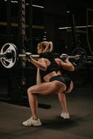 A fit woman with blonde hair is lowering the barbell after squats in a gym photo