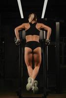 A photo from behind of a woman who is doing push-ups on the uneven bars in a gym