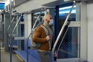 A bald man with a beard in a face mask is leaving a subway car photo