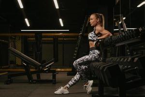 Una foto del lado de una mujer en forma que está sentada en una fila de pesas en el gimnasio