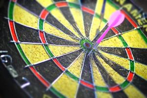 A dart board in black and yellow colors with a pink dart arrow.