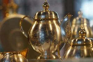 Silver teapot with blackened floral patterns on blurred background. photo