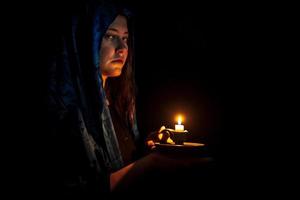 Sad young woman with candle and blue headscarf photo