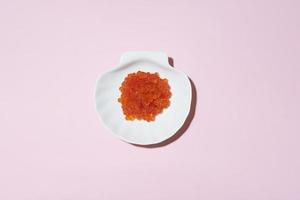 Plato de porcelana con caviar rojo sobre fondo rosa foto