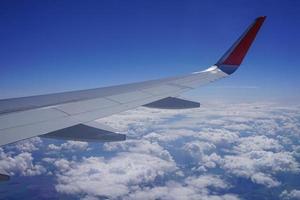 Part of the wing of a plane high in the blue sky among white clouds. photo