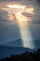 la luz del sol brilla a través del agujero de las nubes a la montaña oscura foto