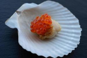 Scallop on a shell with a cap of red caviar. photo