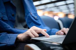 Businessman sitting and using a laptop computer to work at the airport, young person traveling, journey and having internet communication technology for work when waiting indoors at an airport for departure photo