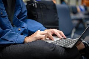 Businessman sitting and using a laptop computer to work at the airport, young person traveling, journey and having internet communication technology for work when waiting indoors at an airport for departure photo