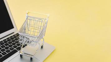 Small cart on laptop on yellow background photo