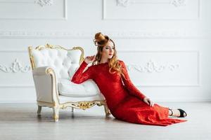 Young girl with red hair in a bright red dress in a bright room photo