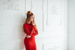 Young girl with red hair in a bright red dress in a light room photo