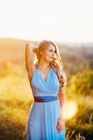 Blonde with loose hair in a light blue dress in the light of sunset photo