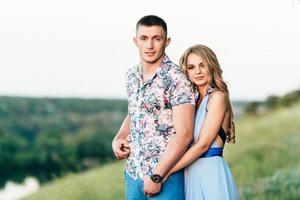 Blonde girl with loose hair in a light blue dress and a guy in the light of sunset photo