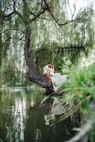 un chico y una chica están sentados juntos en un árbol torcido en la orilla empinada foto