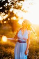 Blonde woman with loose hair in a light blue dress in the light of sunset photo